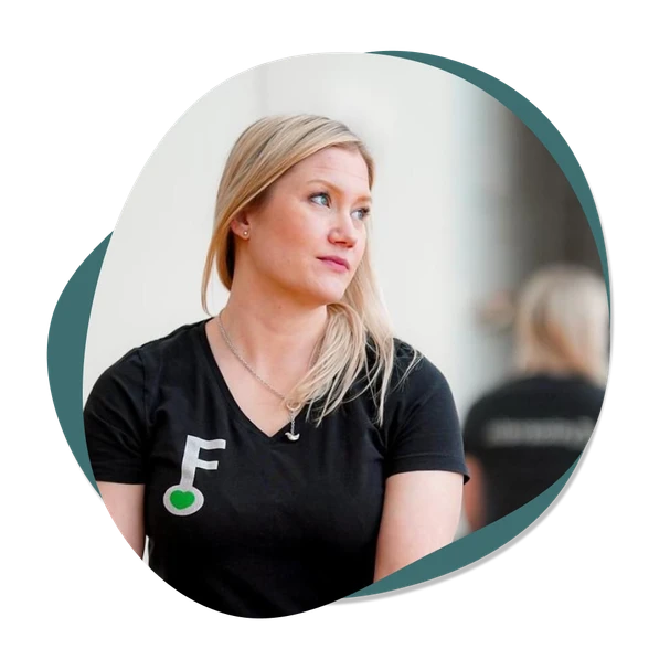 Sari-Anne Kylliäinen - Ammattitaitoinen äitiysfysioterapeutti Tampereella, pukeutunut mustaan t-paitaan, jossa on Fysioavaimen logo, istuu rennosti ja katsoo sivulle mietteliäänä, heijastaen äitiysfysioterapian asiantuntijoiden huomaavainen ja välittävä luonne.
